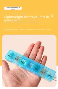 Handheld view of a blue 7-day pill organizer with individual flip lids and weekday labels