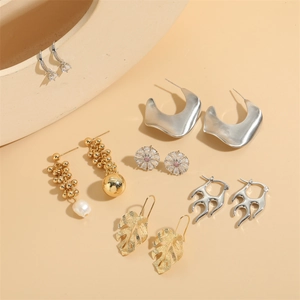 Baroque pearl asymmetric earrings with daisy studs and gold leaves set on beige background