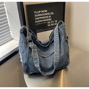 Détail d'un sac cabas en denim bleu avec effet déchiré et boucle en métal réglable
