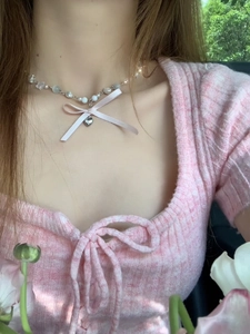 Détail du collier de perles avec nœud rose et pendentif cœur argenté sur le cou