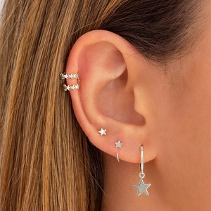 Close-up of a silver star earring set including studs, hoops and ear cuffs on a model