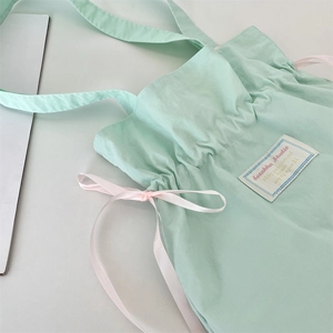 Detail of mint green canvas bag featuring a pink silk bow and stitched brand label