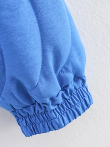 Detail of blue quilted jacket cuff showing elastic wristband and precise stitching