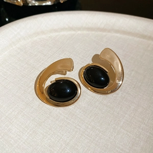Detail view of gold-tone metal earrings with black oval resin stones in spiral design
