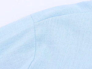 Detail showing the fine stitching and cotton fabric texture of the light blue linen shirt