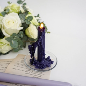 Close-up of a burning deep purple taper candle with melting wax on a clear glass holder