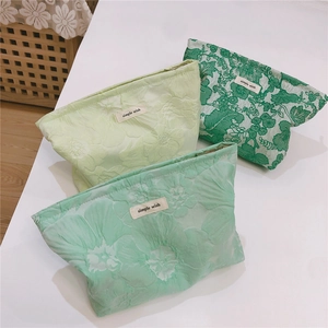 Detailed macro view of three green floral jacquard canvas makeup bags with zip closures