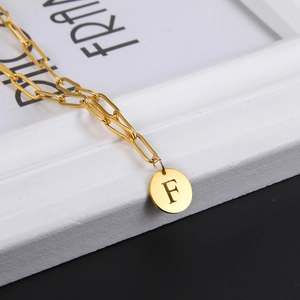 Detailed close-up of golden paperclip chain necklace with round letter F pendant
