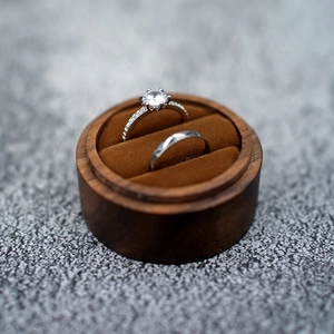 Detail of round black walnut wood ring box with velvet lining holding two elegant rings