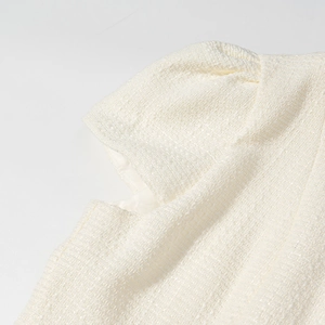 Dettaglio del top in tweed bianco crema con pieghe sulle spalle e trama del tessuto