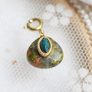 Macro detail of a vintage gold pendant with natural green stone and turquoise inlay on lace