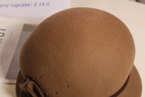 Dettaglio di cappello cloche in feltro di lana con fiocco e perle dorate cammello