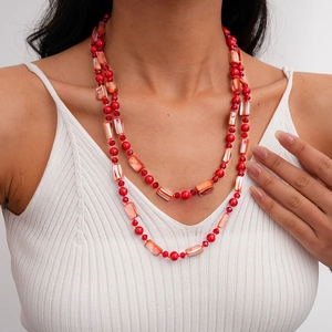 Detail of red beaded necklace with shell slices worn on a white knit sweater