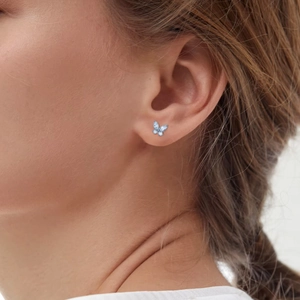 Close-up of a light blue butterfly flat back earring worn on a model earlobe