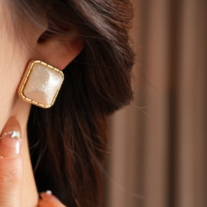 Close-up of a vintage-style gold-plated square earring with a white pearl inlay on ear