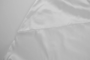 Detailed close-up of premium white satin fabric with smooth silk texture and fine stitching