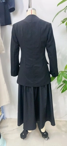 Back view of a stylish black two-piece blazer and long skirt suit for women in a workspace