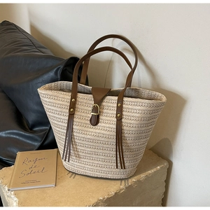 Detail of woven straw texture and brown leather strap on a large beach tote bag