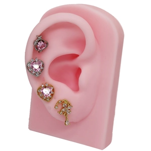 Macro detail of heart-shaped pink zircon cartilage studs and flower tassel earring set