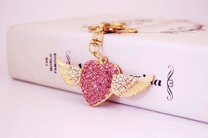 Close-up of golden heart wings keychain featuring sparkling pink rhinestones on a white book