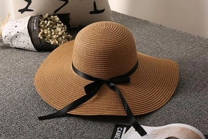 Detail of a dark brown wide-brim straw hat featuring a black satin ribbon and bow