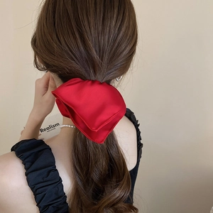 Detail of a large red satin bow hair tie worn on a ponytail with a silky texture