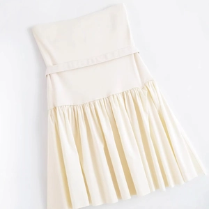 Flat lay of cream tube top dress with belt and elegant pleated skirt detail
