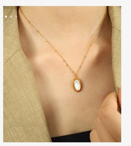 Close-up of golden necklace with oval mother of pearl pendant worn on model neck