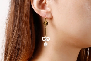 Detail of long drop pearl earring with gold accents and infinity symbol on model