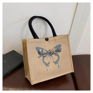 Detail of linen tote bag featuring a blue butterfly pattern and black woven handles