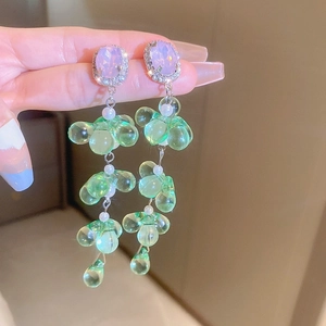 Detail of long fringe earrings featuring purple crystals and green resin flowers