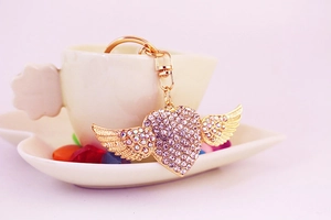 Macro shot of gold heart-shaped keychain with angel wings and pink rhinestones