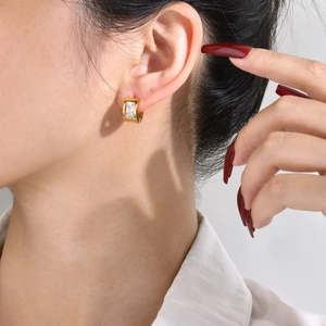 Detail of a gold hoop earring featuring a rectangular emerald-cut clear zircon stone