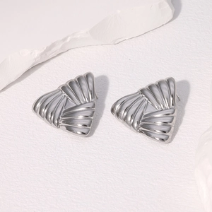 Macro shot of silver triangular stainless steel stud earrings on a white stone texture