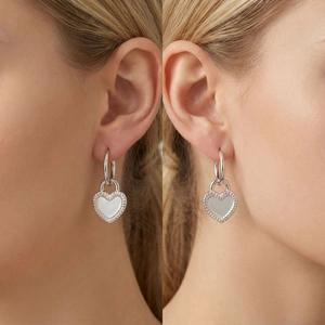 Close-up of model wearing silver heart-shaped hoop earrings with gear-edged design