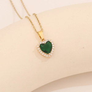 Golden heart necklace with green zircon pendant on minimalist beige background
