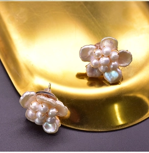Macro shot of baroque pearl flower earrings with gold finish on a metallic tray