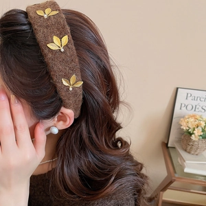 Close-up of brown tweed headband featuring elegant golden leaf metal accents on wavy hair