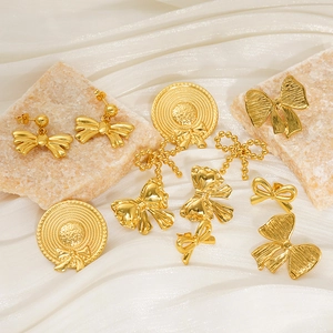 Macro shot of gold bow and sun hat earrings displayed on stone and fabric