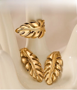 Golden leaf-shaped jewelry set with earrings and ring displayed on a ceramic hand model