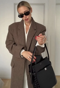 Detailed view of women's long dark brown wool coat and black crocodile pattern handbag