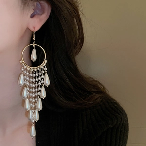 Detail of long tassel earrings with drop pearls and gold metal rings worn by a model
