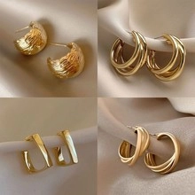 Set di quattro orecchini geometrici dorati su elegante tessuto di seta color champagne