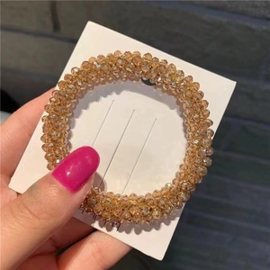 Detail of a champagne beaded elastic hair tie held against a minimalist background
