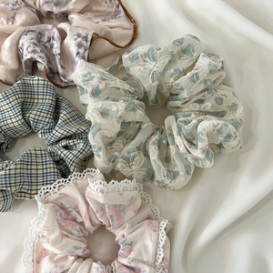 Flat lay of four diverse scrunchies including floral lace and silk patterns on fabric