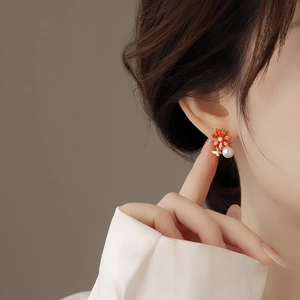 Détail de boucles d'oreilles fleur, pétales orange, perle blanche et papillon doré