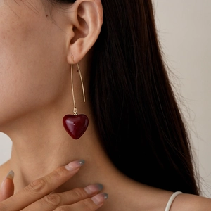 Close-up of elegant gold long-hook earrings with deep red heart-shaped resin charms