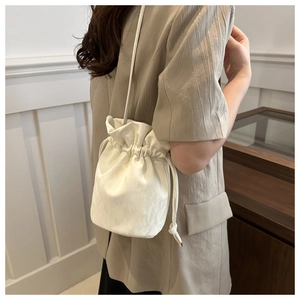 Close-up of white silk fabric bucket bag with drawstring showing refined satin texture