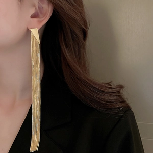 Close-up of golden long tassel triangle earrings worn by a model in a black suit