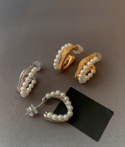 Close-up of gold and silver C-shaped earrings with pearls and crystals on dark texture